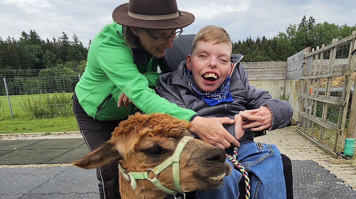 Bild von Stefanie Hagner mit einem Kind im Rollstuhl und einem Alpaka